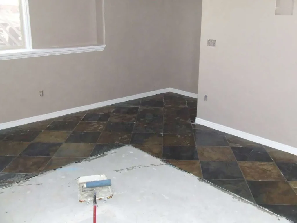 image shows a room with partially installed slate floor tiles and a paint roller
